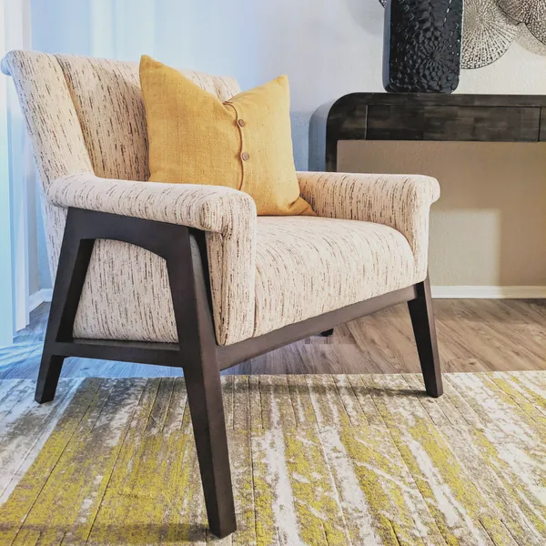 Mid-century accent chair in textured upholstery with a mustard linen pillow and an abstract rug