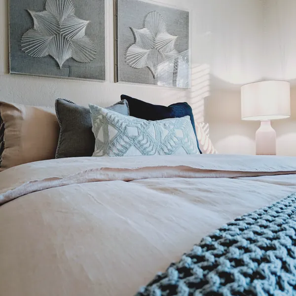 Bed styled with linen bedding, layered blue pillows and string art panels above