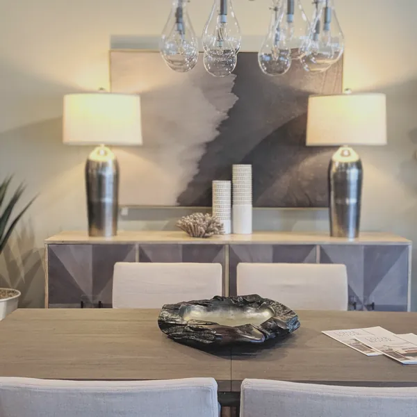 Dining room with a glass teardrop chandelier, linen chairs and a geometric sideboard with silver lamps