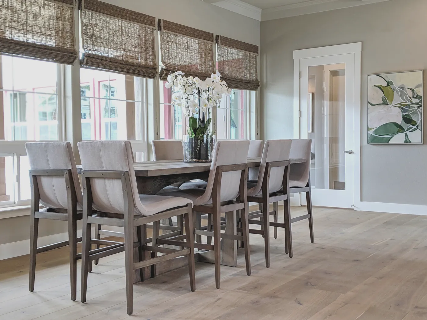 Dining room with linen counter stools, a rustic wood table, woven bamboo shades and white orchids, designed by Consult Interiors