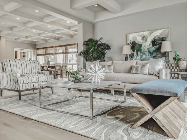 Living room with a coffered ceiling, linen sofa, striped armchair, abstract art and a sculpted wool rug