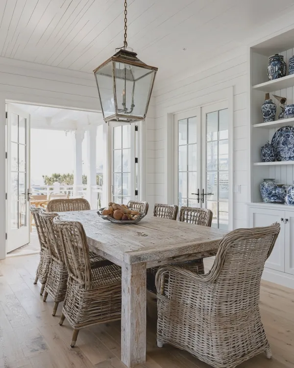 Design rendering of a coastal dining room with a whitewashed farmhouse table, wicker chairs, glass lantern and blue and white porcelain