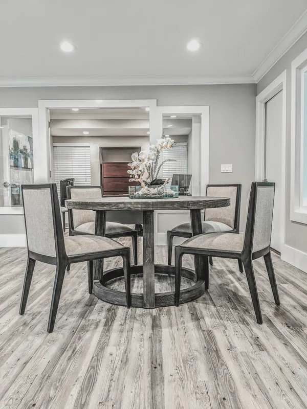 Round wood dining table with upholstered chairs and an orchid centerpiece on gray plank floors