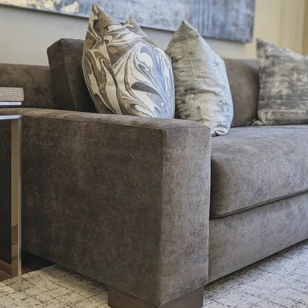 Gray velvet sofa with marbled and textured pillows beside a chrome side table
