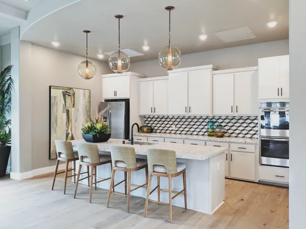 White kitchen with glass globe pendants, woven counter stools and a geometric tile backsplash